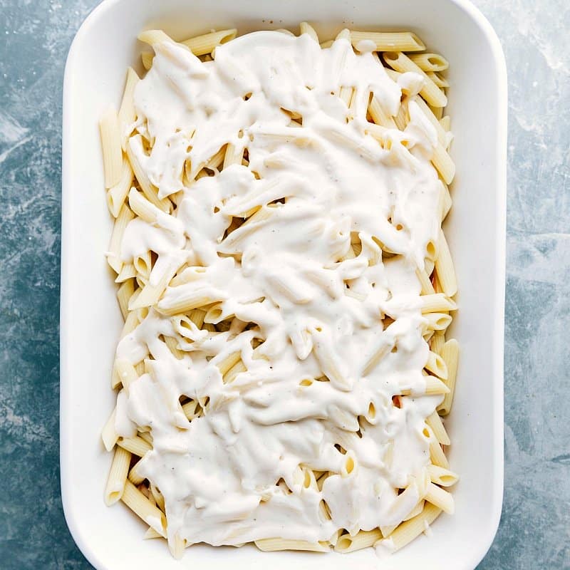 Adding White Sauce to Pasta Casserole - Preparing for Baking White sauce being poured over a casserole full of noodles, ready for baking.