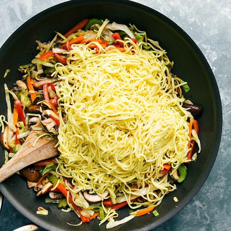 Combining Noodles with Vegetables in Skillet for Chow Mein Adding noodles to the skillet filled with vegetables.