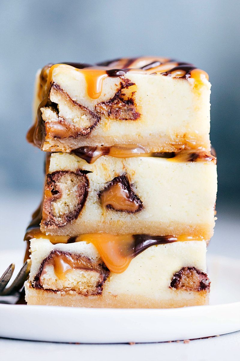 The BEST EVER Twix Cheesecake Bars with an easy (2-ingredient) caramel sauce and chocolate ganache. Everyone goes crazy over this dessert! chelseasmessyapron.com #twix #cheesecake #bars #caramel #chocolate #sauce #ganache #shortbread #crust #easy #dessert #desserts #kidfriendly #cheesecakes Stack of three Twix Cheesecake Bars