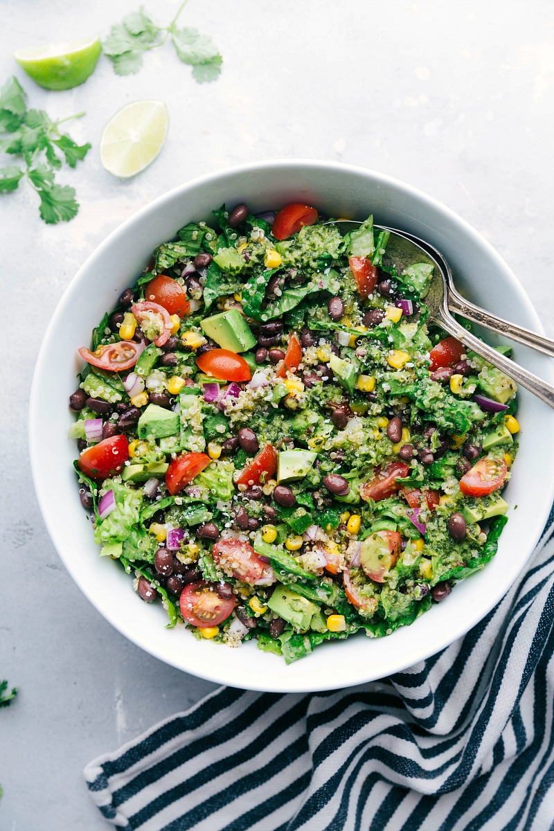 Flavorful and Healthy Southwest Quinoa Salad A bowl filled with a flavorful and healthy southwest quinoa salad, accompanied by two serving spoons on the side.