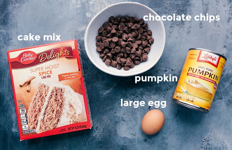 Ingredients for Cake Mix Pumpkin Cookies Ingredients laid out, including a box of cake mix, chocolate chips, a can of pumpkin puree, and an egg.