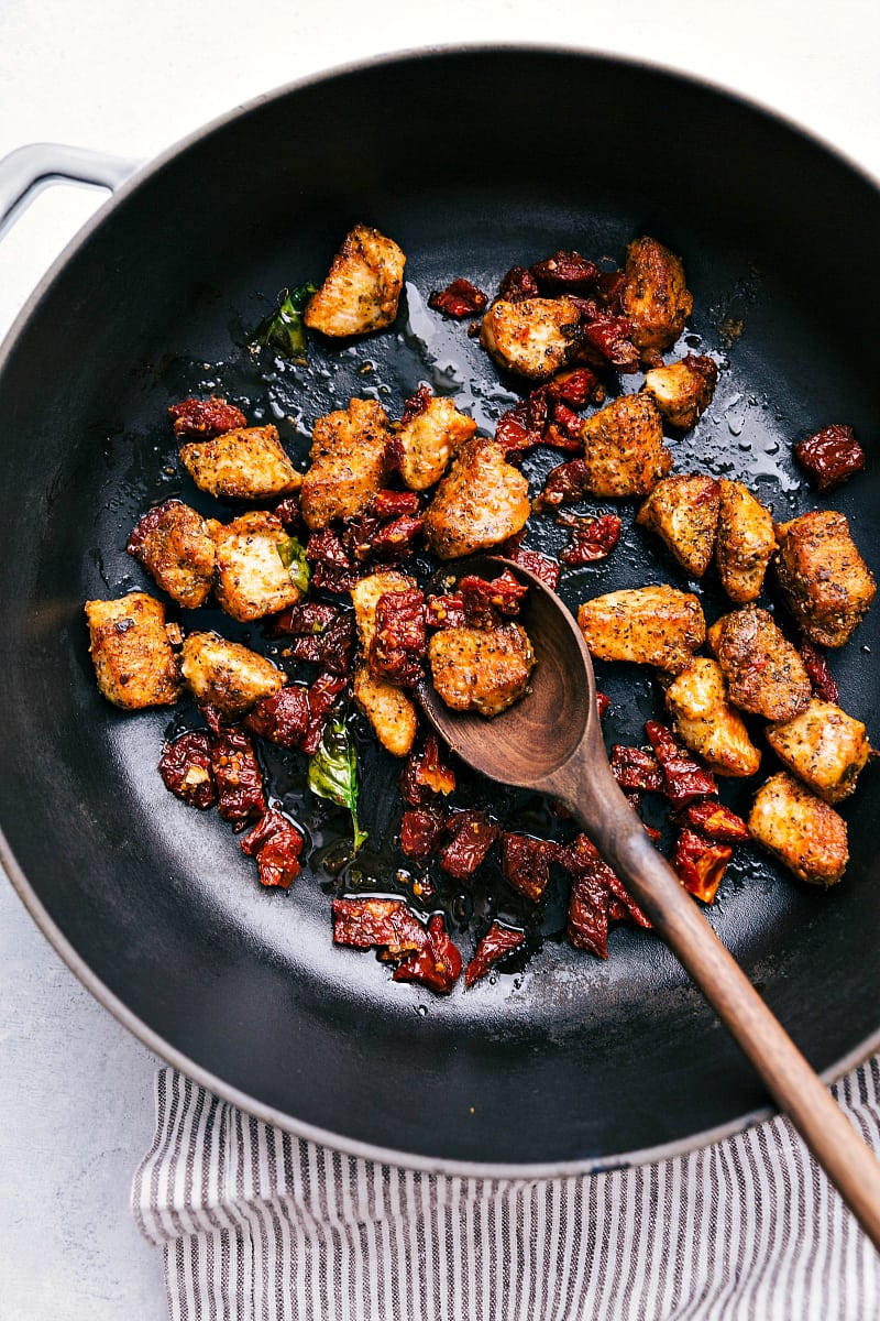 You'll love this one-pot, easy and quick Pesto Chicken Tortellini with sun-dried tomatoes and fresh basil! Recipe via chelseasmessyapron #recipes #pastasalad #greencolors #pesto #chicken #sundriedtomatoes Process shot-- Overhead image of the chicken and sun-dried tomatoes being cooked in the pot.