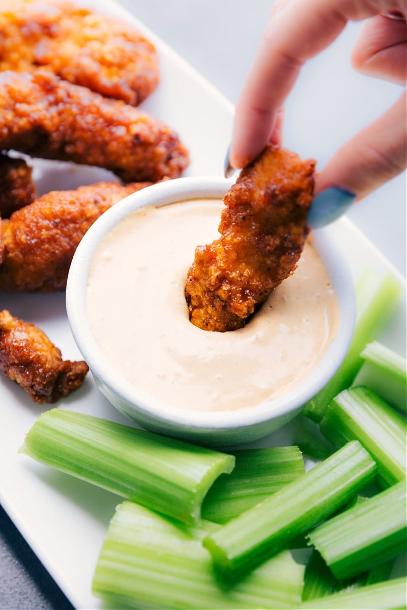 Chipotle Ranch Dip is an explosion of flavor and has a great kick of spice! Add everything to a blender and let it rip. Recipe via chelseasmessyapron #gameday #best #spicy #quick #easy #simple #blender #chipotle #ranch #dip Image of a piece of chicken being dipped into the Chipotle Ranch Dip