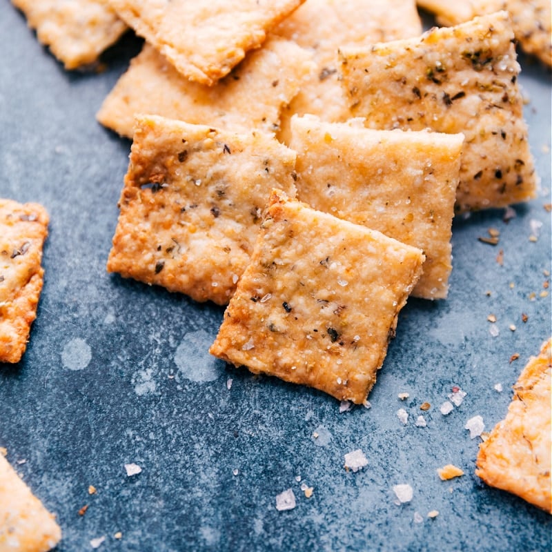 We're obsessed with these Homemade Crackers made with Parmesan cheese and Italian seasoning. Making crackers from scratch may seem excessive or intimidating, but we've simplified the process and are delivering a drool-worthy recipe. Once you try it, you won't forget it! Recipe via ChelseasMessyApron #snack #quick #easy #simple #best #homemade #crackers Image of a stack of Homemade Crackers ready to be eaten