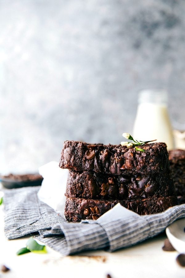 This rich Chocolate Zucchini Bread is moist, deeply chocolatey, and completely irresistible! This zucchini bread also uses better-for-you ingredients — less sugar than most zucchini bread, Greek yogurt, dark chocolate, coconut oil, blended-up oats, and of course, grated zucchini. Recipe via chelseasmessyapron #dessert #cocoa #healthy #breakfast #milk #chocolate #zucchini #bread Chocolate Zucchini Bread slices stacked on top each other