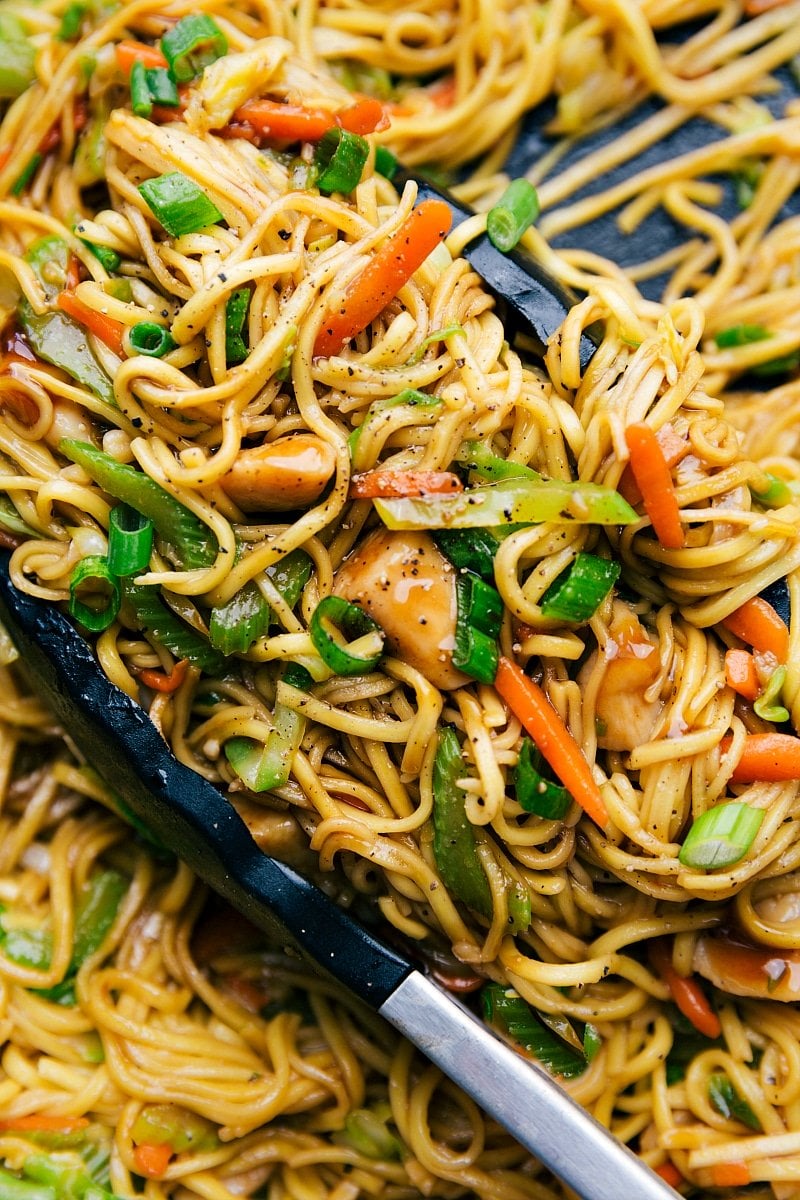 Chicken chow mein in a skillet with tongs, filled with fresh vegetables, perfectly cooked and seasoned.