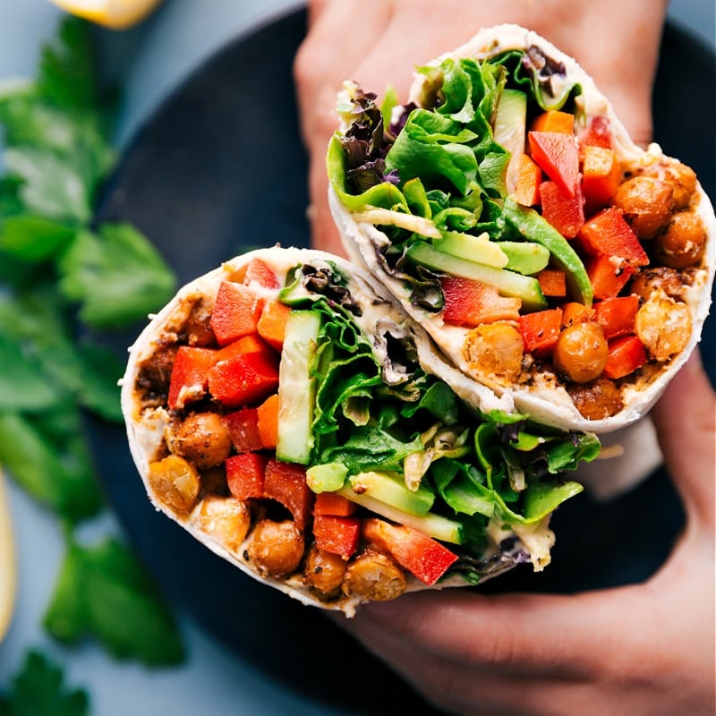 30-Minute Hummus Wrap Hummus wrap cut in half, showing chickpeas, fresh veggies, and sauce inside.