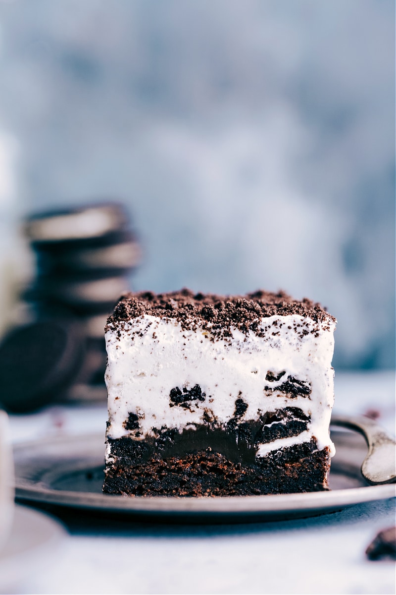 This Brownie Oreo Ice Cream Cake is one for the books! Fudge-y rich brownies are topped with chopped Oreo cookies that have been smothered in hot fudge and get topped with Cookies & Cream ice cream. Add a layer of whipped topping with a few more crushed Oreos for good measure -- more is more with this dessert! Recipe via chelseasmessyapron #dessert #best #quick #easy #simple #birthday #frozen #frozendessert #oreo #icecream #cake Image of a piece of Brownie Oreo Ice Cream Cake on a plate