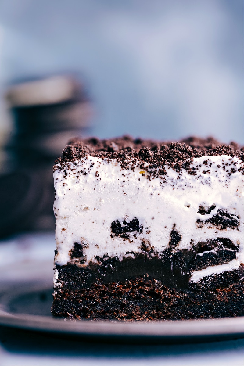 This Brownie Oreo Ice Cream Cake is one for the books! Fudge-y rich brownies are topped with chopped Oreo cookies that have been smothered in hot fudge and get topped with Cookies & Cream Ice Cream. Recipe via chelseasmessyapron #dessert #best #quick #easy #simple #birthday #frozen #frozendessert #oreo #icecream #cake Up-close image of a slice of the Brownie Oreo Ice Cream Cake, ready to be eaten.