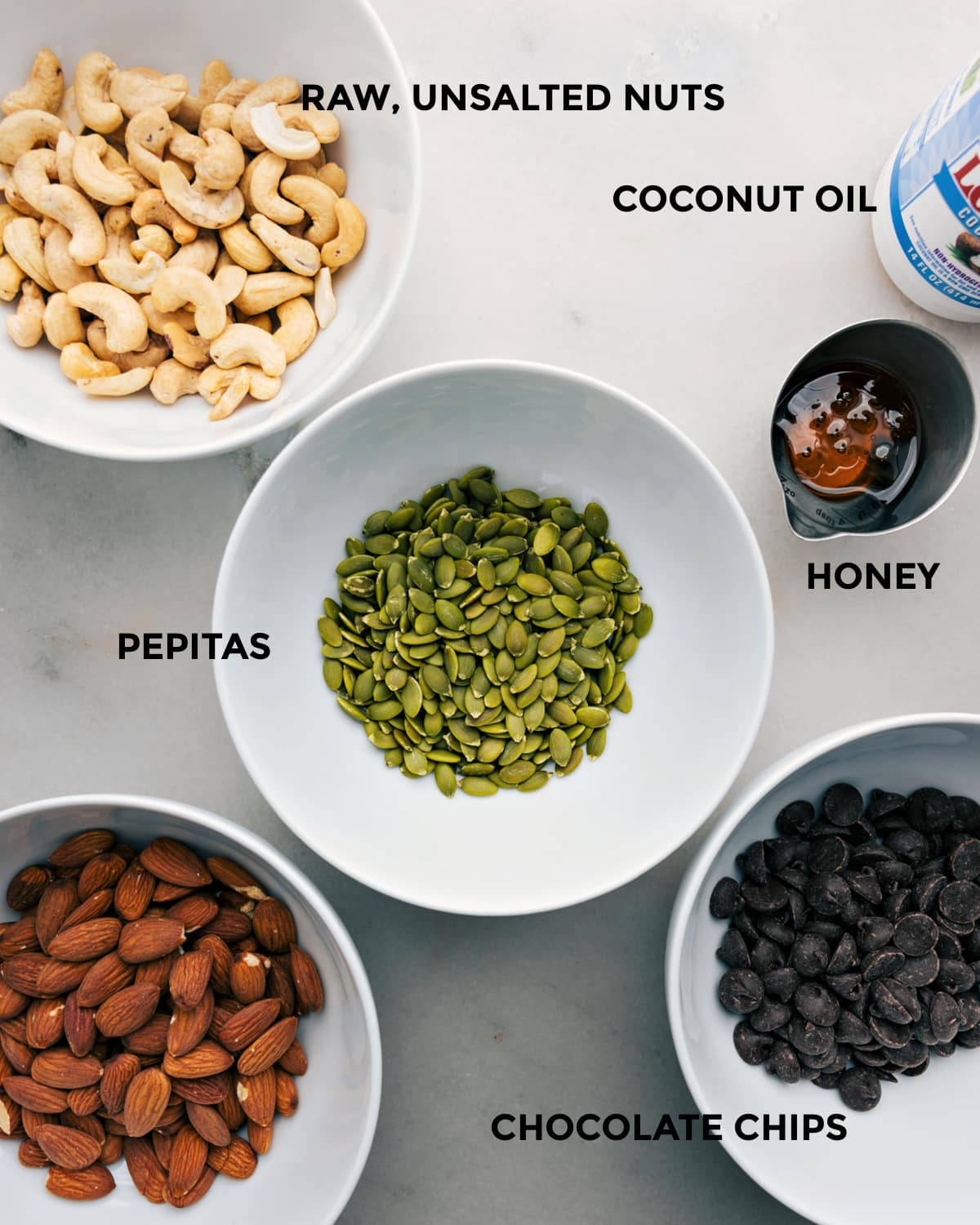 Ingredients In This Delicious Healthy Nut Bark All the ingredients in this recipe like nuts, coconut oil, pepitas, honey, and chocolate chips prepped out for easy assembly.