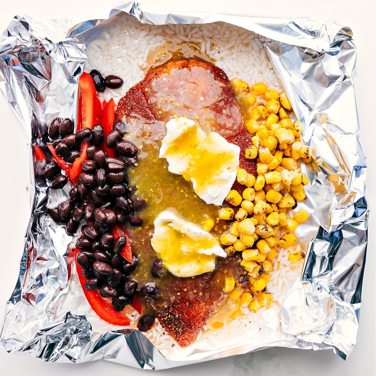 Flavorful And Delicious Chicken Rice Foil Packs Foil packet filled with rice, corn, beans, cream cheese, salsa verde, and chicken, ready to be cooked over a fire, grill, or in the oven.