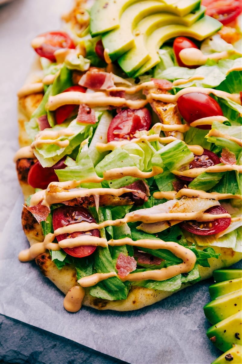 This Chipotle Chicken Flatbread starts with soft, warmed naan with melty pepper-jack cheese and rotisserie chicken. Once out of the oven, we top it with some iceberg lettuce, cherry tomatoes, and ripe, creamy avocados. A sprinkling of crispy bacon and drizzle of the most addicting chipotl- ranch dressing and you're in dinner heaven! Recipe via chelseasmessyapron #dinner #quick #easy #simple #best #oven #sauce #chipotle #chicken #flatbread Chipotle Chicken Flatbread