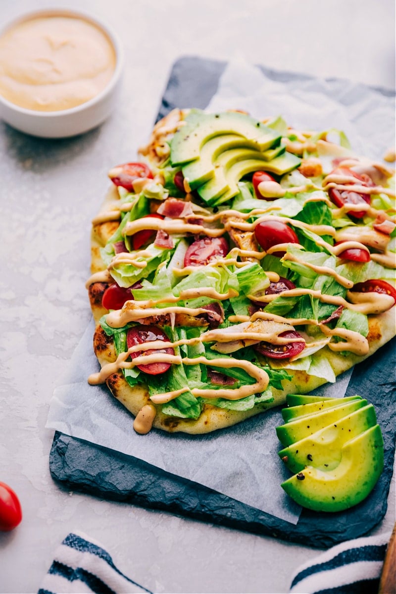This Chipotle Chicken Flatbread starts with soft, warmed naan with melty pepper-jack cheese and rotisserie chicken. Once out of the oven, we top it with some iceberg lettuce, cherry tomatoes, and ripe, creamy avocados. A sprinkling of crispy bacon and drizzle of the most addicting chipotl- ranch dressing and you're in dinner heaven! Recipe via chelseasmessyapron #dinner #quick #easy #simple #best #oven #sauce #chipotle #chicken #flatbread Chipotle Chicken Flatbread