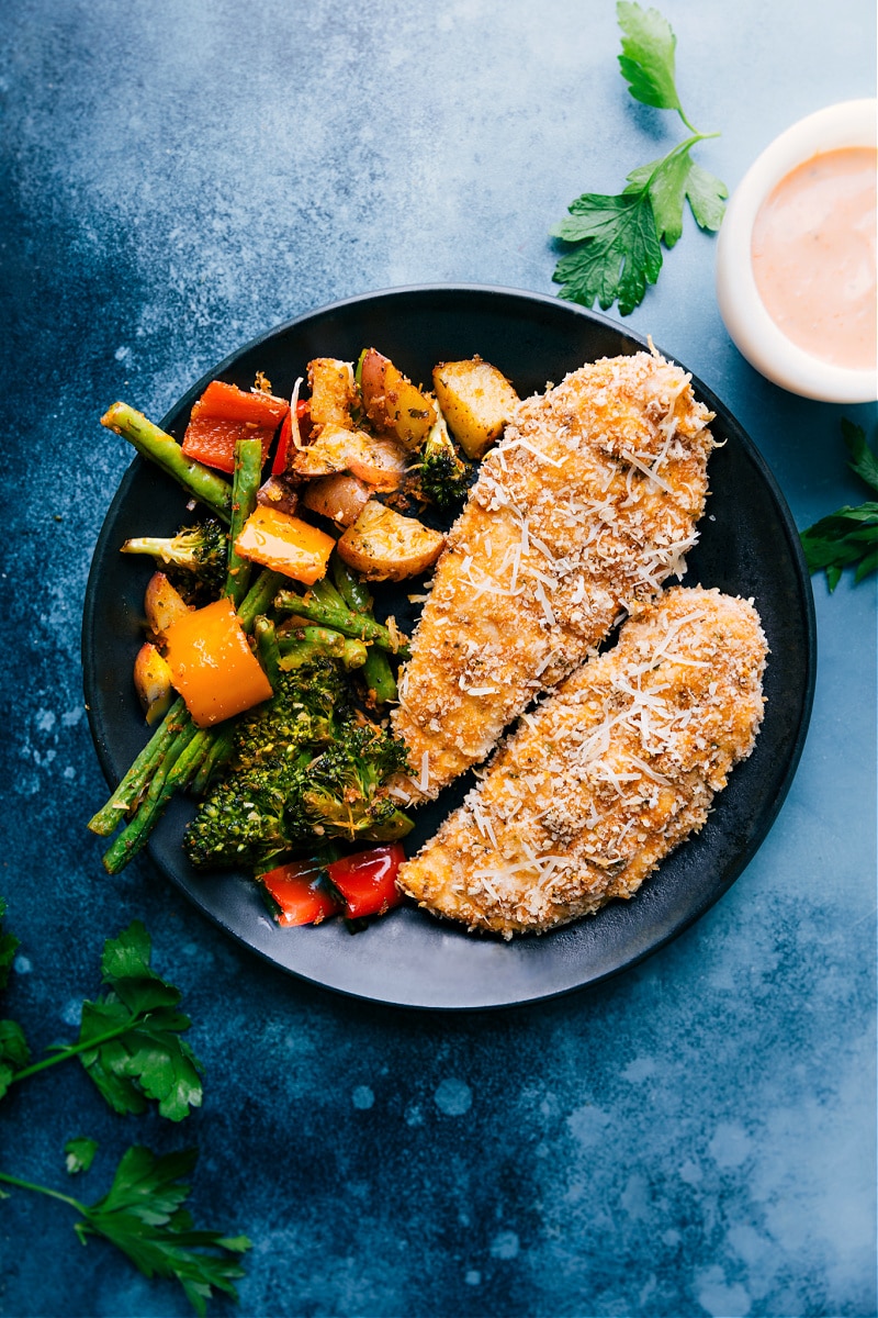 The Best Baked Parmesan Chicken Tenders Baked parmesan chicken tenders on a plate with veggies on the side.