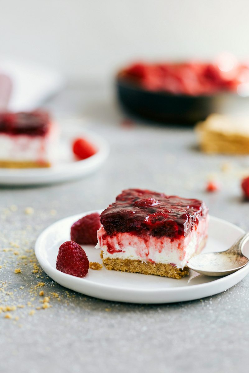 This Raspberry Jello Dessert is our all-time favorite! A variation on the famous "strawberry pretzel salad", but with a thick graham cracker crust and raspberries instead. This is a simple-to-make and crowd-pleasing treat or addition to your holiday table. Recipe via ChelseasMessyApron #sidedish #treat #best #quick #easy #simple #creamcheese #grahamcracker #raspberry #jello #dessert Image of the Raspberry Jello Dessert on a plate