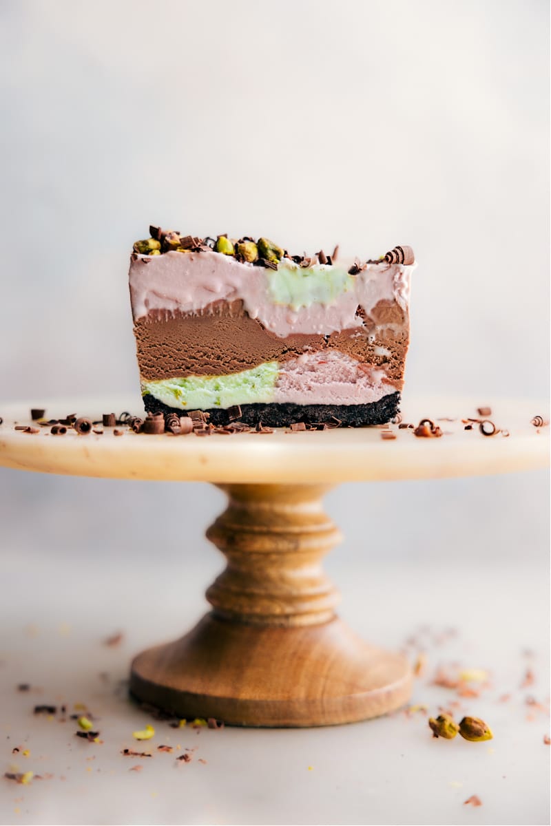 This is a simplified Spumoni recipe using store-bought ice cream in cherry, chocolate (or vanilla), and pistachio flavors. The combination of these three flavors is unbelievably good! The ice creams are alternately layered in a lined bread loaf pan, creating a vibrant and flavorful dessert. To serve, the Spumoni is sliced into bars, offering a wonderful blend of flavors in every bite. This recipe is a quick, easy dessert option, perfect for impressing guests or for a fun family treat. Recipe via chelseasmessyapron #dessert #best #quick #easy #simple #frozen #nobake #icecream #treat #Neapolitan #summerdessert #spumoni Image of sliced Spumoni on a cake stand