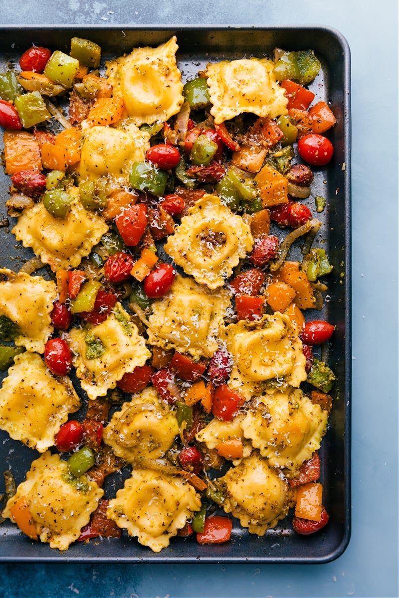Pesto Ravioli combines perfectly caramelized roasted veggies with tender cheese-filled ravioli and loads of fresh basil pesto. Top each bowl with a drizzle of olive oil, lots of freshly grated Parmesan cheese, and another spoonful of pesto for an unforgettableย pasta dish! Recipe via ChelseasMessyApron #dinner #quick #easy #simple #roasted #veggies #onetray #tomatoes #pesto #ravioli Pesto Ravioli on a tray