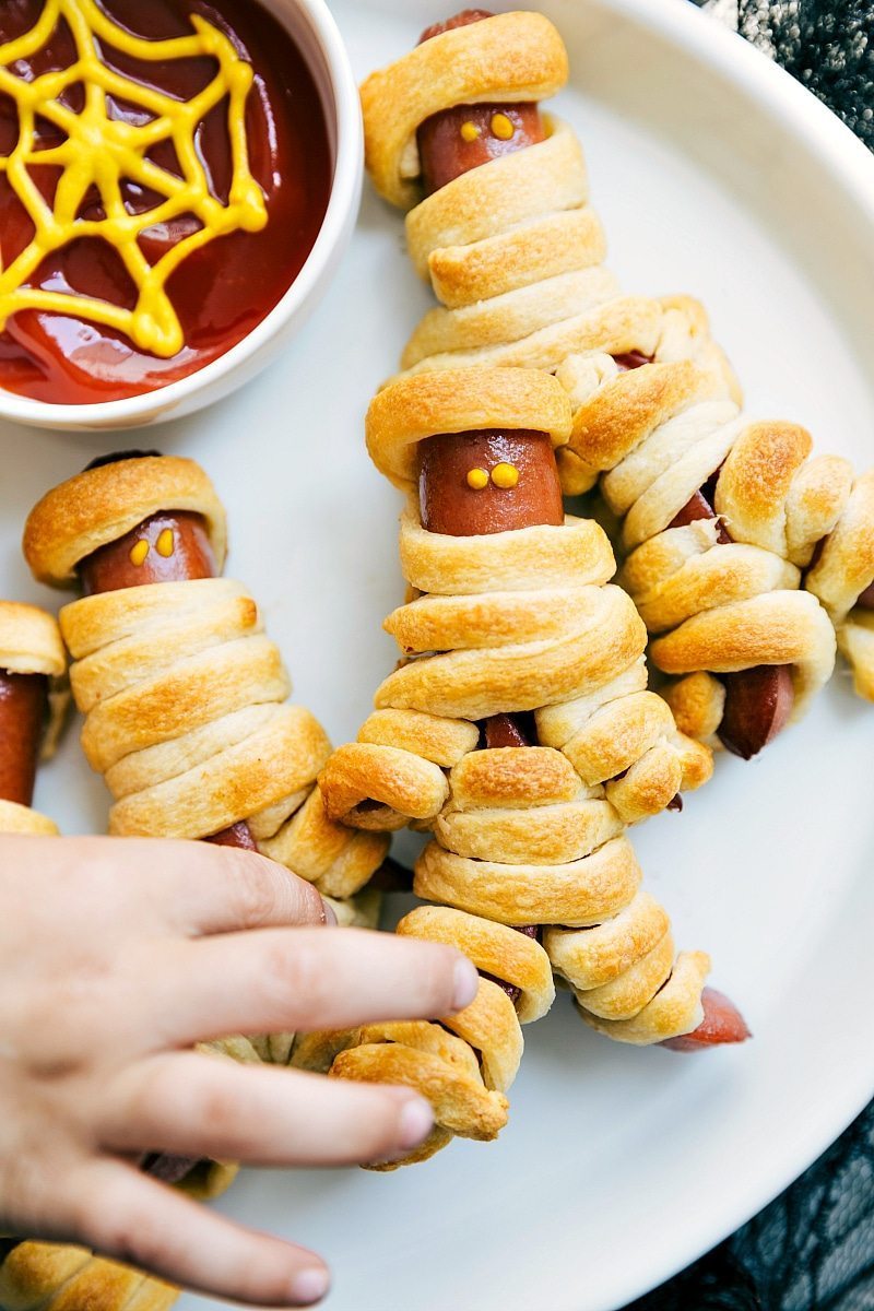 Four easy, & creative Halloween party appetizers that are so delicious -- Spiderweb 7-Layer Dip, Walking Dead Mummy Dogs, Monster Meatball Sliders, & Cheesy Monster Fingernail Bread. chelseasmessyapron.com #mummy #hotdog #mustard #halloween #treats #appetizer Image of the walking dead mummy dogs that go along with these easy halloween appetizers