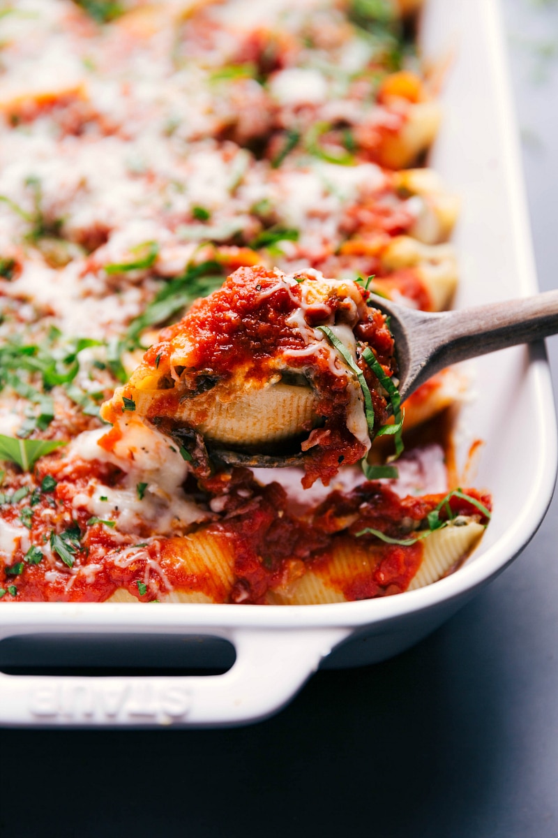 Serving Hearty Stuffed Shells with Italian Sausage - A Savory Delight A serving spoon scooping out a hearty portion of savory stuffed shells with italian sausage from a baking dish.