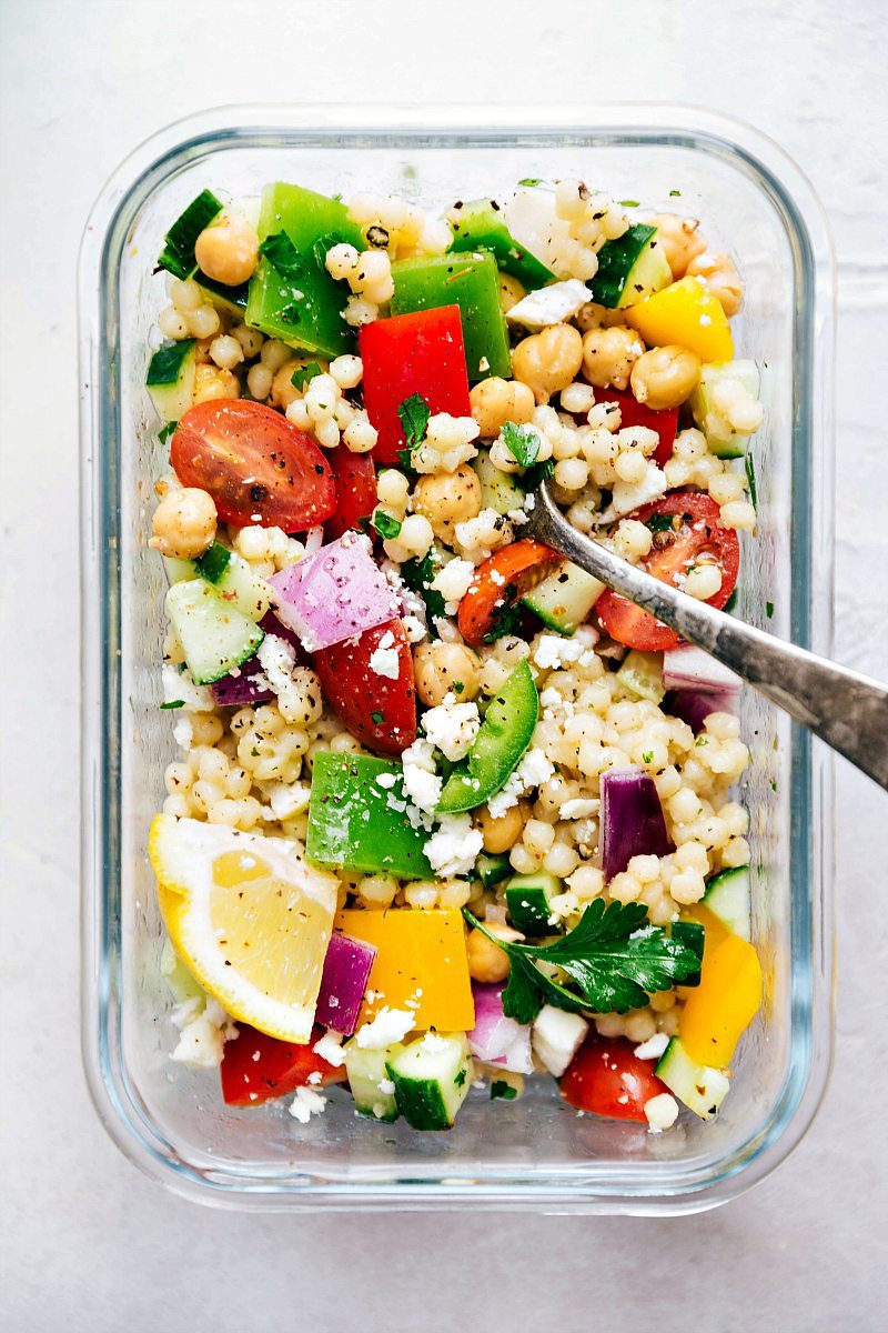 Greek Salad With Couscous For Dinner Greek couscous salad dressing and tossed together with a fork in it ready to be enjoyed.