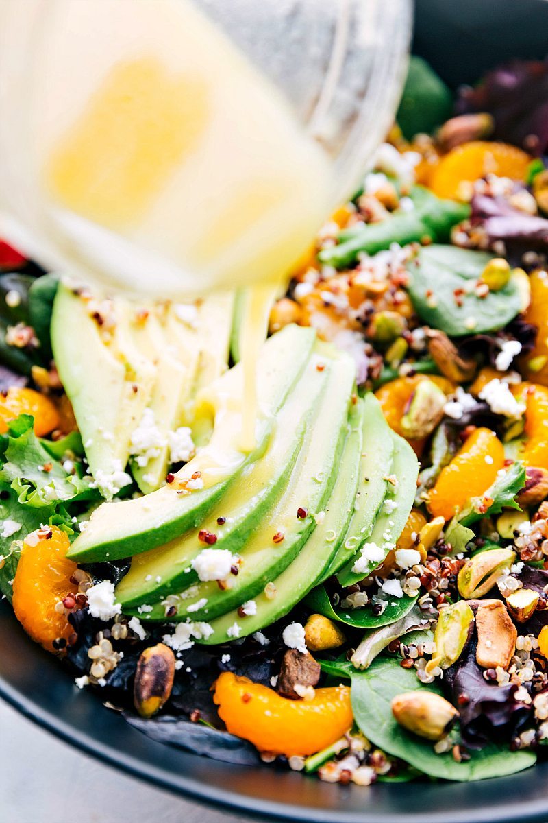 This salad is drizzled with a tangy and sweet citrus vinaigrette. Recipe via chelseasmessyapron #healthy #detox #clean #whole #mixedgreens #nutrients #pistachio #citrus #quinoa #salad Up-close image of the dressing being poured over the Citrus Quinoa Salad.
