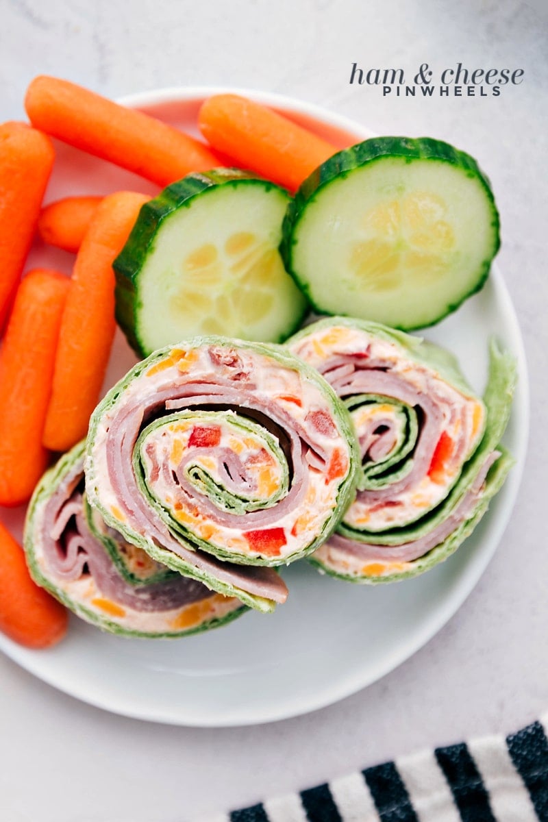 Ham and Cheese Pinwheels on a plate with fresh cucumbers and carrots for a well-rounded lunch.