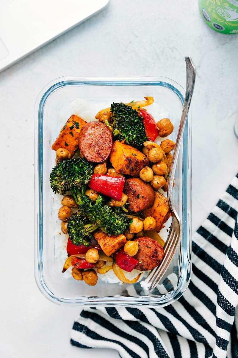 You're going to love Sausage and Chickpeas! They are tossed with onions, sweet potatoes, broccoli, and a sweet bell pepper in an unforgettable Mexican-inspired seasoning blend. This meal is prepared on one sheet pan requiring minimal prep time and even quicker clean-up! Recipe via ChelseasMessyApron #broccoli #onions #peppers #sausage #chickpeas Image of Sausage and Chickpeas in a meal prep container showing different options for this recipe.