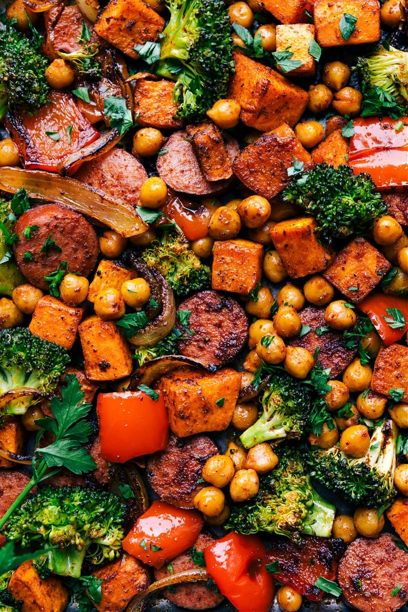 Sausage and Chickpeas are tossed with onions, sweet potatoes, broccoli, and a sweet bell pepper in an unforgettable Mexican-inspired seasoning blend. This meal is prepared on one sheet pan requiring minimal prep time and even quicker clean-up! Recipe via ChelseasMessyApron #broccoli #onions #peppers #sausage #chickpeas Overhead image of Sausage and Chickpeas