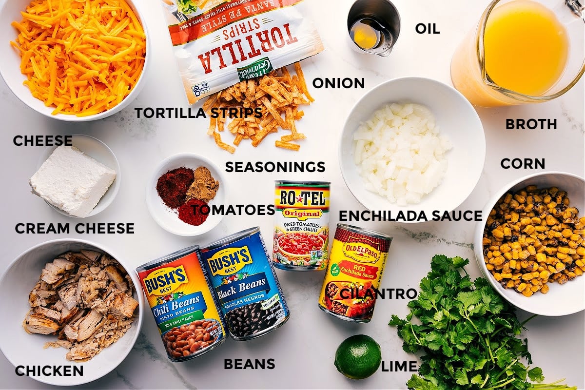 Ingredients In Chicken Tortilla Soup Recipe Chicken Tortilla Soup ingredients prepped and ready to assemble, including cheese, tortilla strips, cream cheese, chicken, beans, tomatoes, cilantro, onion, lime, enchilada sauce, corn, broth, oil, and seasonings.