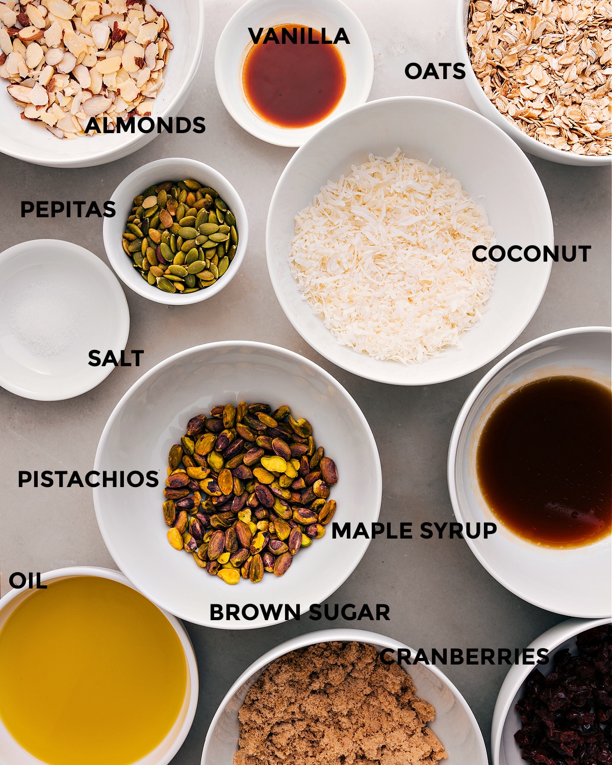 Ingredients In Homeamde Granola All the ingredients in this recipe are prepped for easy assembly: coconut, oats, vanilla, almonds, pepitas, maple syrup, pistachios, salt, brown sugar, cranberries, and oil.