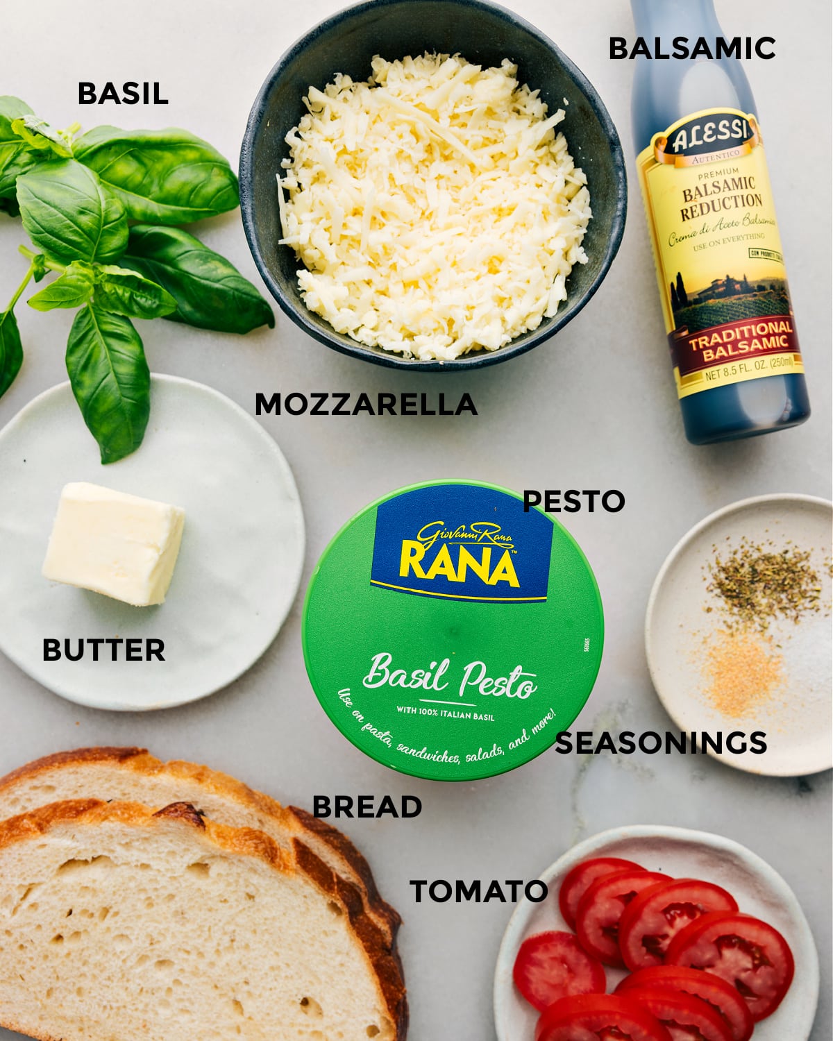 Ingredients In Caprese Grilled Cheese The ingredients in this recipe prepped for easy assembly including basil, balsamic, mozzarella, pesto, butter, seasonings, tomato, and bread.