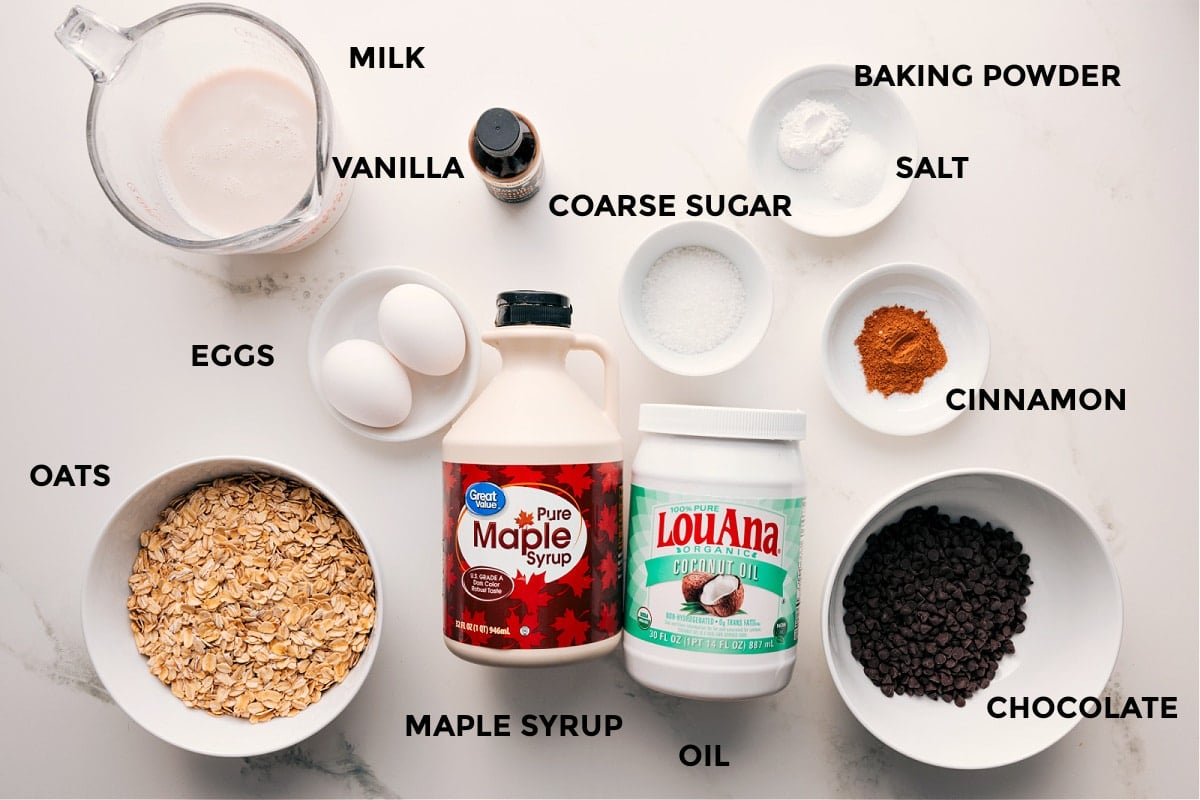 Ingredients In Chocolate Chip Baked Oatmeal Ingredients in this recipe prepped out for easy assembly including milk, vanilla, oats, eggs, maple syrup, oil, chocolate, cinnamon, baking powder, salt, and coarse sugar.
