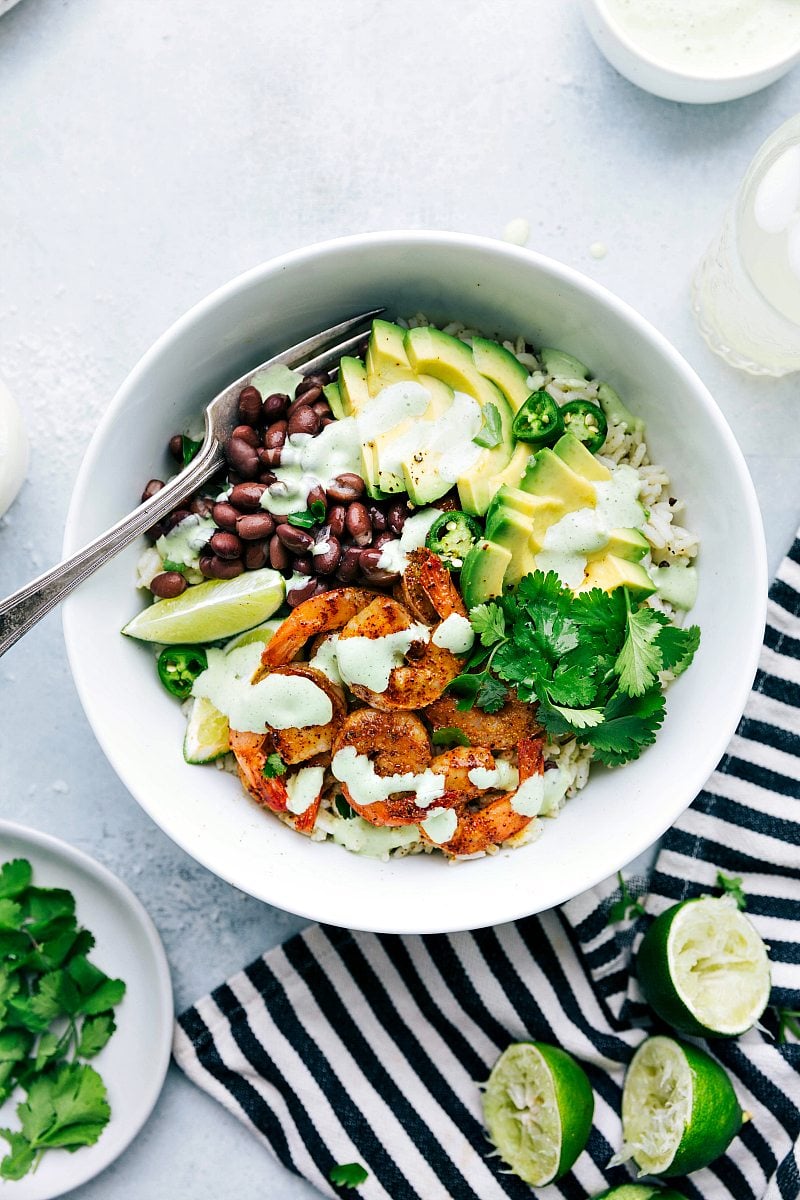 Seasoned and succulent shrimp atop cilantro-lime rice with savory black beans, creamy avocados, and a show-stopping cilantro-lime sauce. This high-protein meal is nutritious, nourishing, filling, and best of all packed with flavor. Recipe via ChelseasMessyApron #dinner #quick #easy #simple #best #healthy #clean #cleaneating #wholefoods #familyfriendly #kidfriendly #cilantro #lime #shrimp #bowl Up-close overhead image of the Cilantro Lime Shrimp ready to be served