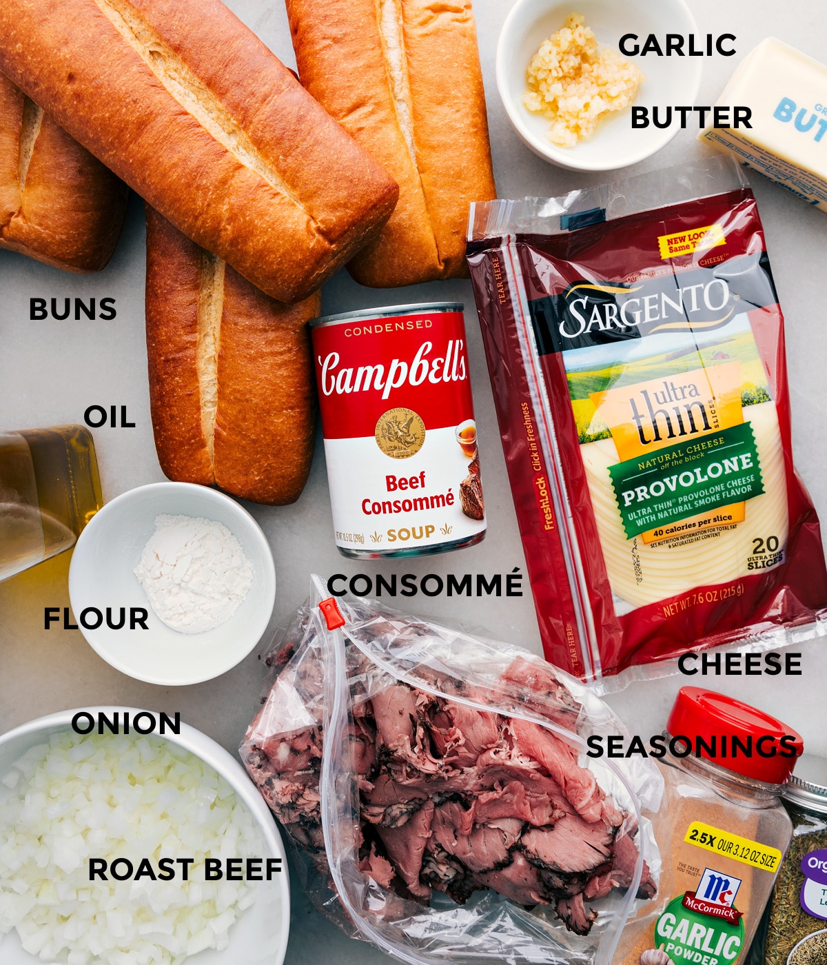 Ingredients In 15 Minute Easy French Dip Sandwiches All the ingredients including buns, oil, flour, onions, roast beef, garlic, butter, cheese, seasonings, and consomme prepped out for easy assembly.