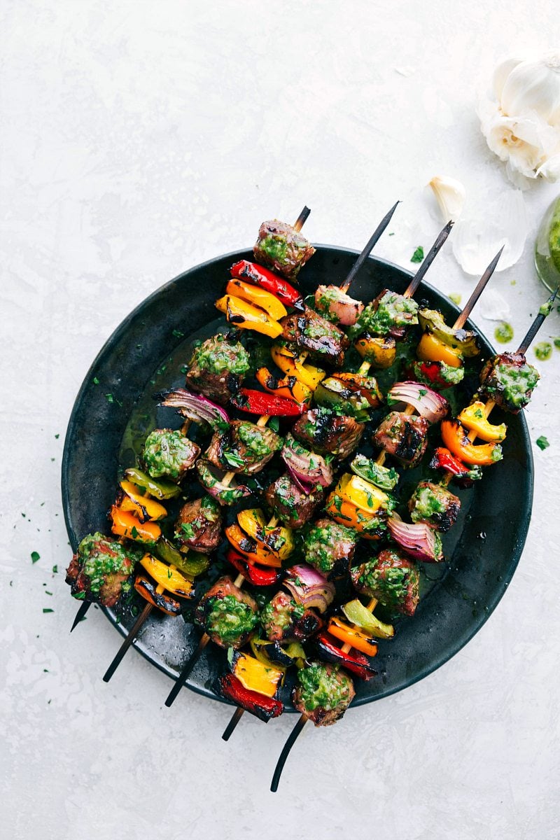 Thick cut pieces of steak are marinated in a flavorful blend of ingredients and then skewered with peppers and onion and then grilled to perfection to bring you the best steak kebabs! Plate of steak kebabs with basil sauce on top.