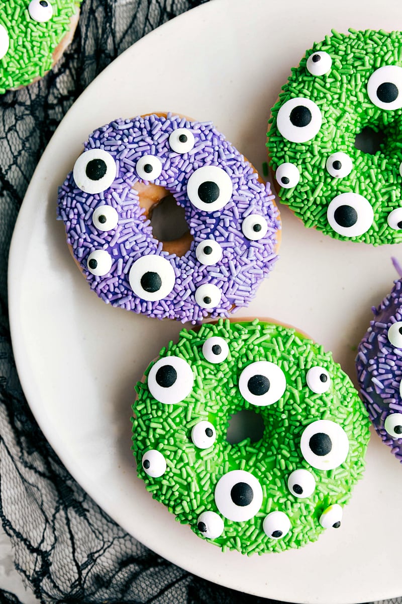 The Monster Halloween Donuts on a Plate Covered with Purple and Green Sprinkles and Candy Eyes The monster Halloween donuts on a plate covered with purple and green sprinkles and candy eyes.