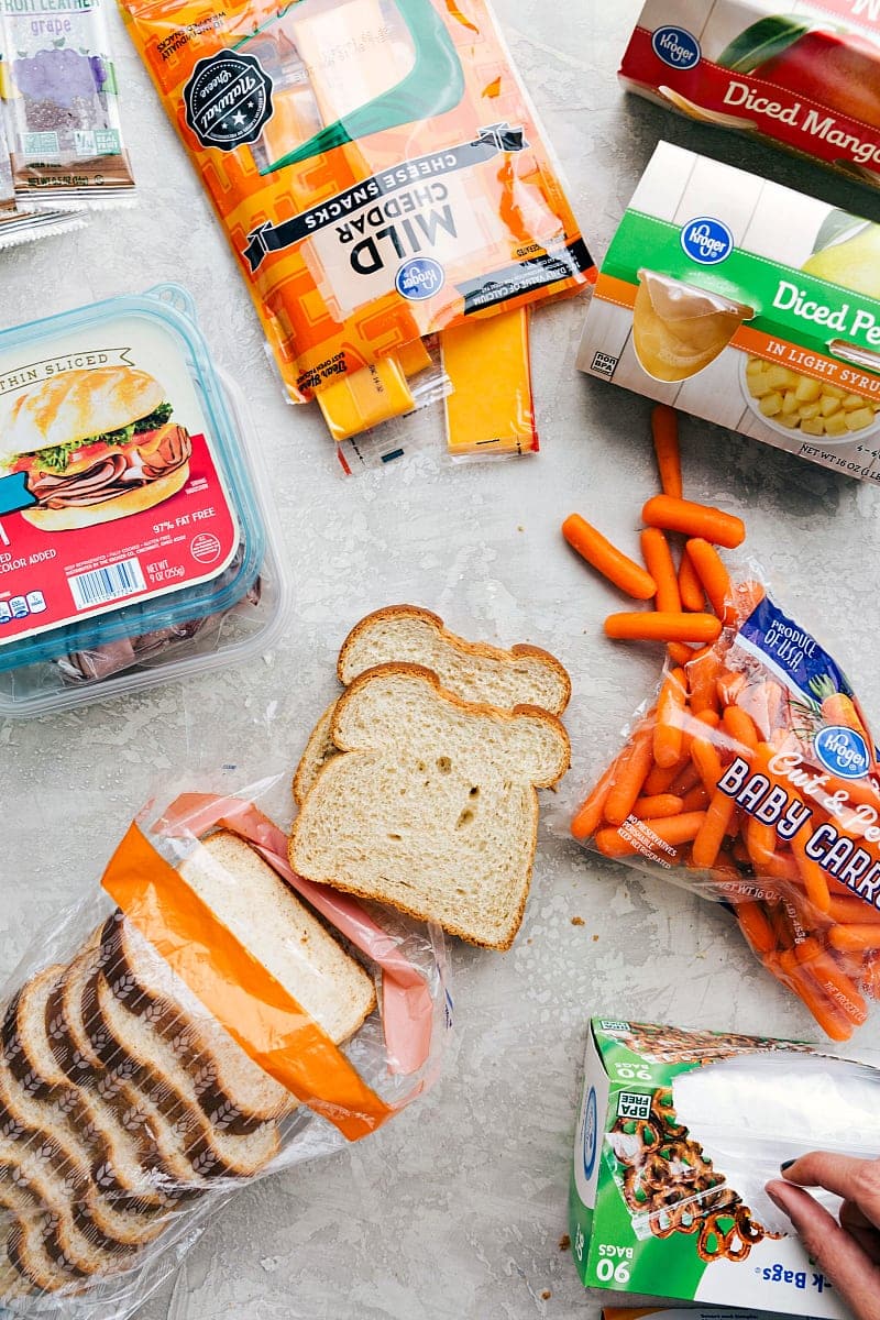 Packed Lunch with Deli Meat, Cheese, and Snacks Sliced deli meat, cheese, fruit, bread, veggies, and a fruit snack, all packed together for a nutritious and balanced school lunch idea for kids.