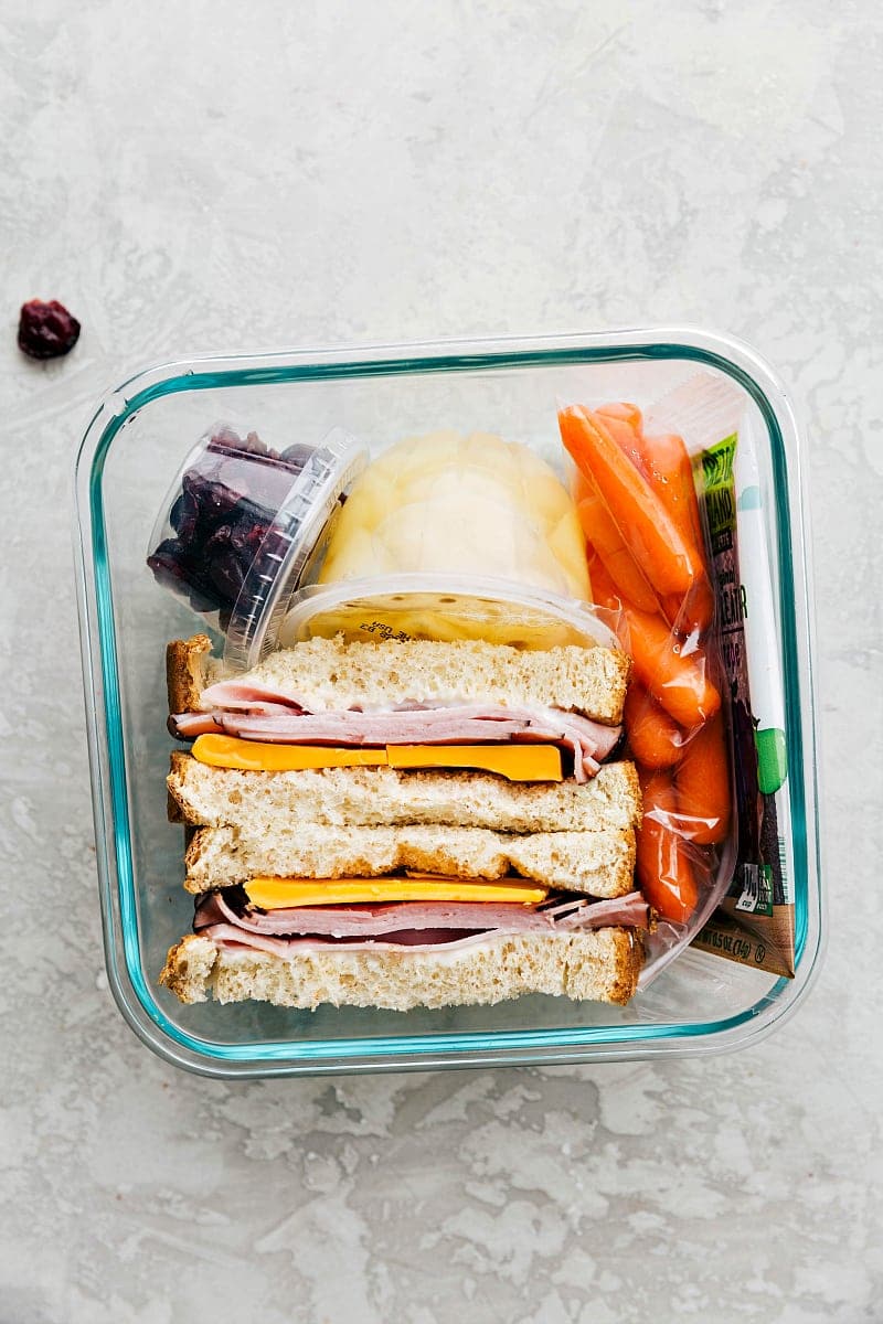 Packed Lunch with Sandwich, Fruit, Veggies, and Snack A meat and cheese sandwich, fresh fruit, veggies, and a snack, all packed in a container and ready to go.
