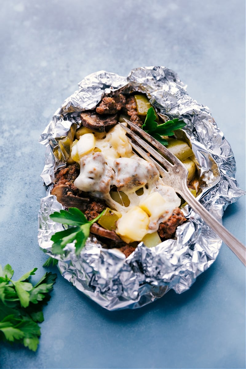 Philly Cheesesteak Foil Packs make a fun campfire meal. These foil packs are loaded with veggies -- onion, peppers, potatoes, and mushrooms. On top of the veggies, we add seasoned and crumbled ground beef and finish everything off with gooey melted Provolone cheese. Recipe via ChelseasMessyApron #dinner #quick #easy #simple #best #cheesy #peppers #potatoes #campfire #phillycheesesteak #foilpacks Philly Cheesesteak Foil Packs