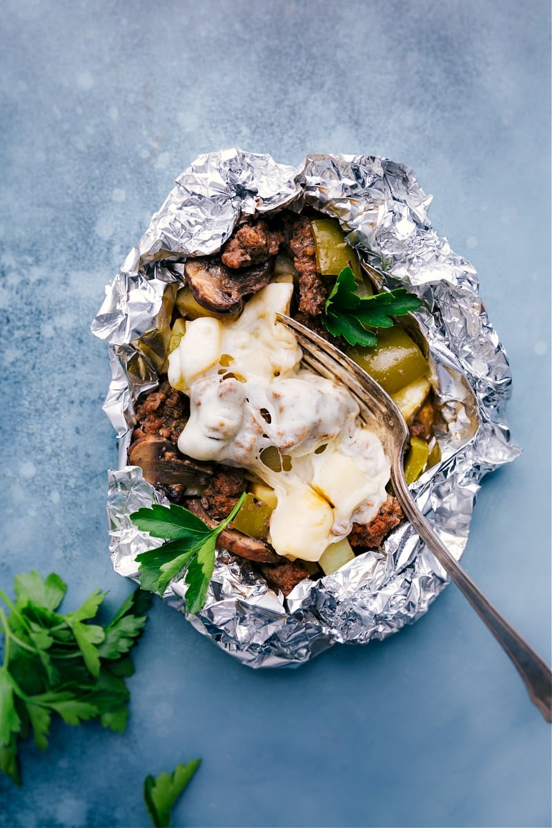 Philly Cheesesteak Foil Packs make a fun campfire meal. These foil packs are loaded with veggies -- onion, peppers, potatoes, and mushrooms. On top of the veggies, we add seasoned and crumbled ground beef and finish everything off with gooey melted Provolone cheese. Recipe via ChelseasMessyApron #dinner #quick #easy #simple #best #cheesy #peppers #potatoes #campfire #phillycheesesteak #foilpacks Philly Cheesesteak Foil Packs