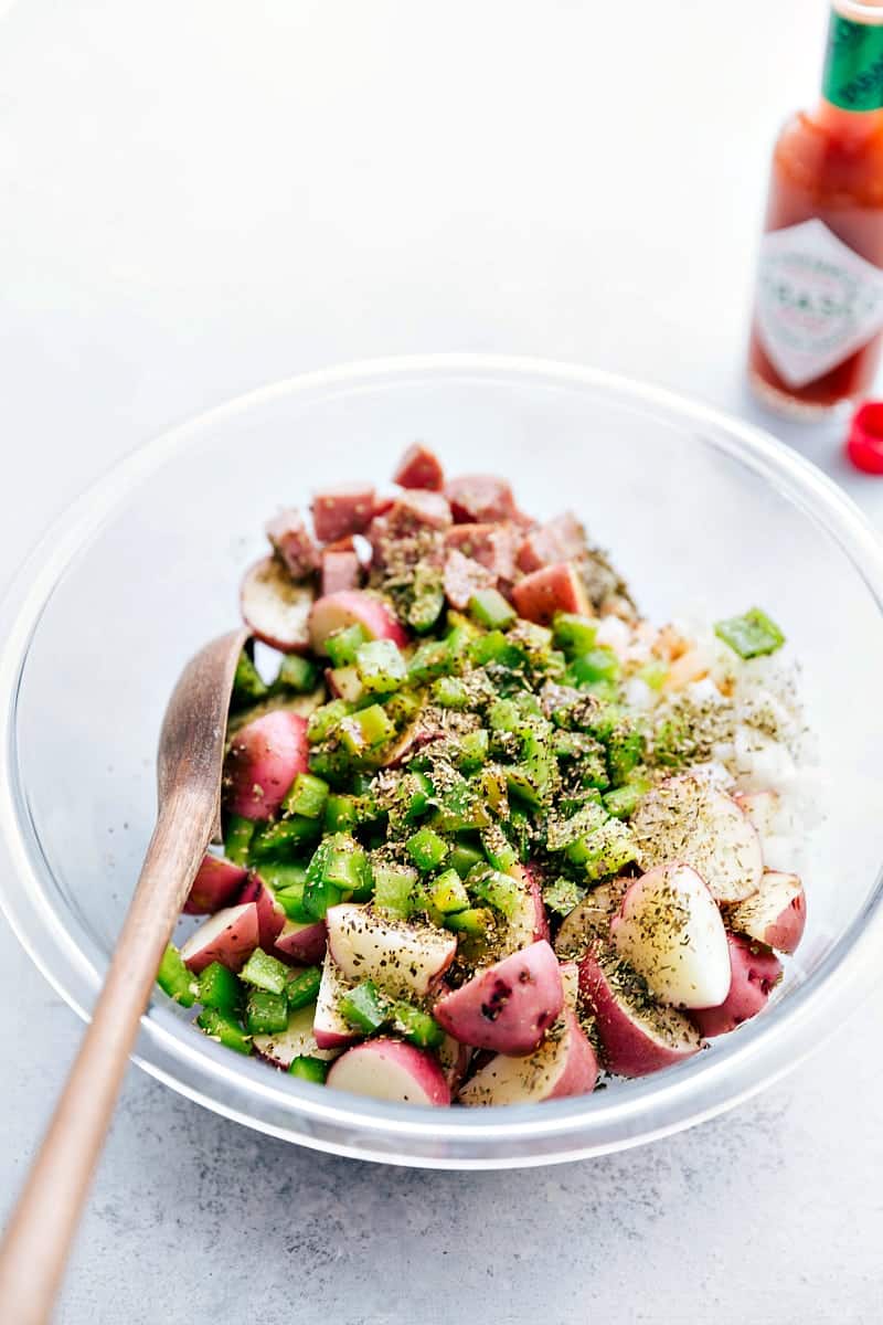 How To Make Sausage And Potato Foil Packs All the veggies, sausages, and seasonings added to a bowl to toss together.