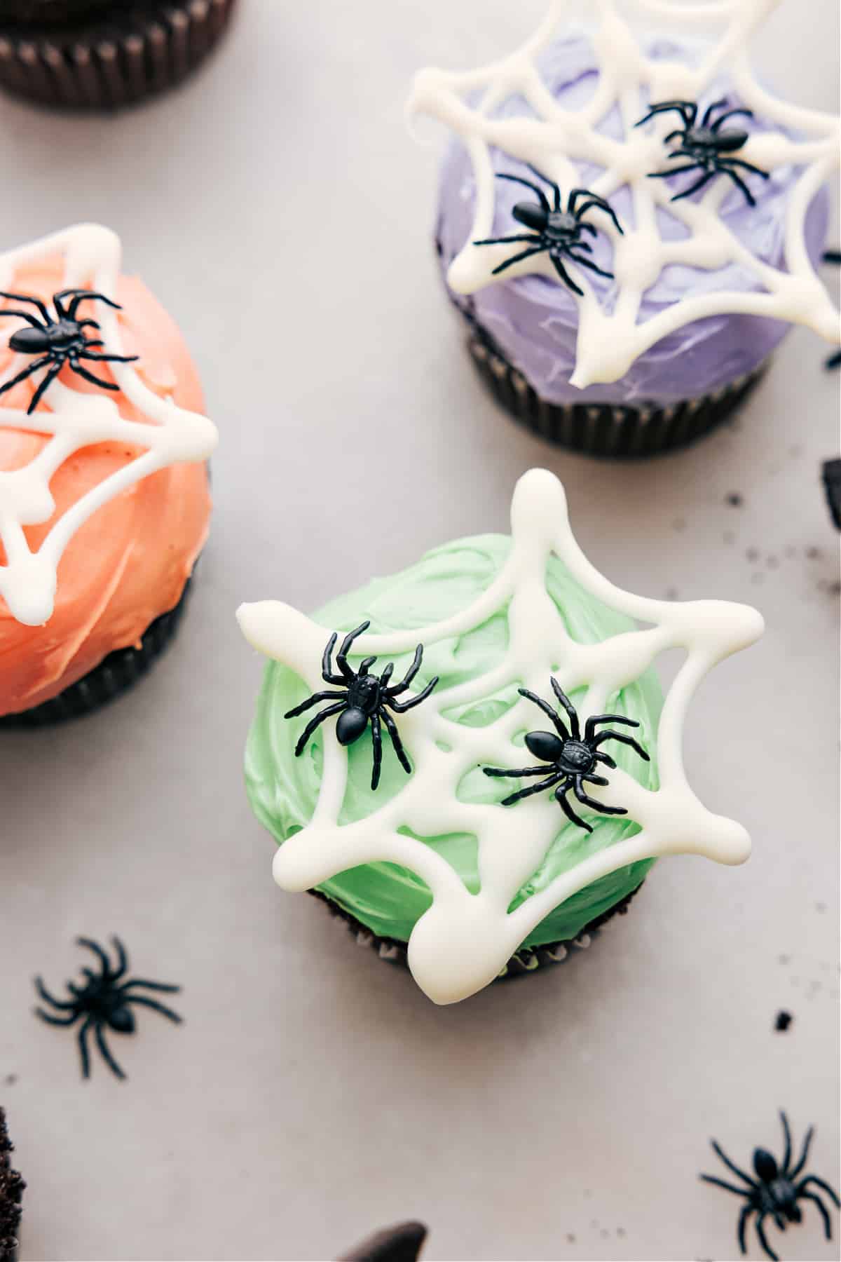 Easy And Fun Spider Cupcakes Spider web with fake spiders on colored frosting.