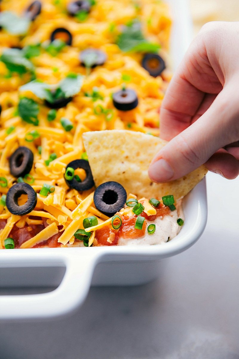 Ready-to-eat 7 layer bean dip being dipped into with a chip.