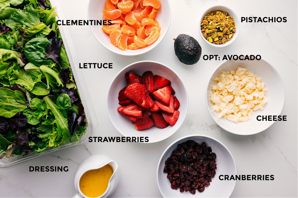 Ingredients In Strawberry Salad Recipe All ingredients prepped for easy assembly, including the fruit, pistachios, avocado, cheese, cranberries, dressing, and lettuce.
