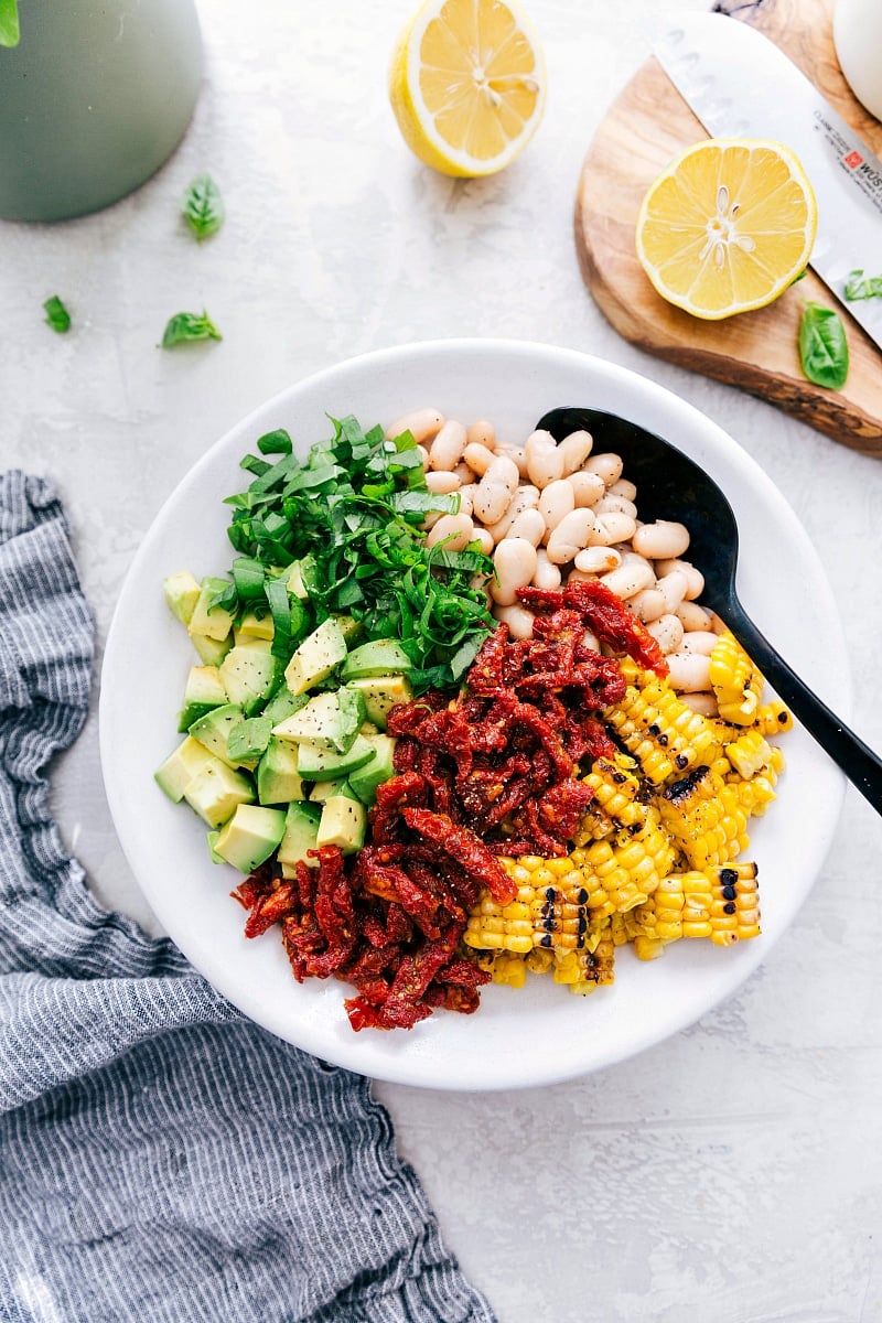 This White Bean Salsa with creamy avocado, crisp corn, savory sun-dried tomatoes, fresh lemon, and sweet basil is our latest obsession! It's perfect over grilled Pesto Chicken, quinoa, or couscous (hello crave-able vegetarian meal!), or with some good tortilla chips. Recipe via Chelseasmessyapron #healthy #keto #whole #protein #whole30 #best #avocado #corn #sundriedtomatoes #clean #cleaneating #whitebean #salsa White Bean Salsa ingredients
