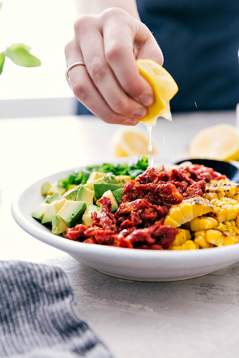The best ever White Bean Salsa with creamy avocado, crisp corn, savory sun-dried tomatoes, fresh lemon, and sweet basil is our latest obsession! It's perfect over grilled Pesto Chicken, quinoa, or couscous (hello crave-able vegetarian meal!), or with some good tortilla chips. Recipe via Chelseasmessyapron #healthy #keto #whole #protein #whole30 #best #avocado #corn #sundriedtomatoes #clean #cleaneating #whitebean #salsa Drizzling lemon juice over the White Bean Salsa.