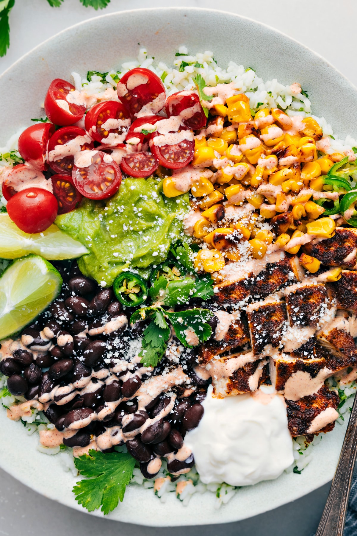 This Burrito Bowl Recipe Is The Perfect Meal Prep Burrito bowl recipe with cilantro-lime rice, black beans, corn, guacamole, tomatoes, and a chili-lime sauce drizzle.