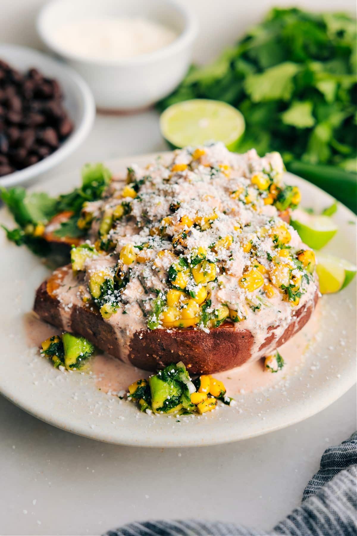 This Mexican Street Corn-inspired Loaded Sweet Potato is an easy oven-baked sweet potato with a delicious mix of corn, green onions, cilantro, jalapeño, lime, Mexican cheese, and a creamy sauce. Recipe via Chelseasmessyapron.com #sweetpotato #vegetarian #loaded #streetcorn #elote #Mexican #healthy Mexican streeet corn loaded sweet potatoes topped with the most delicious sauce and cotija cheese.