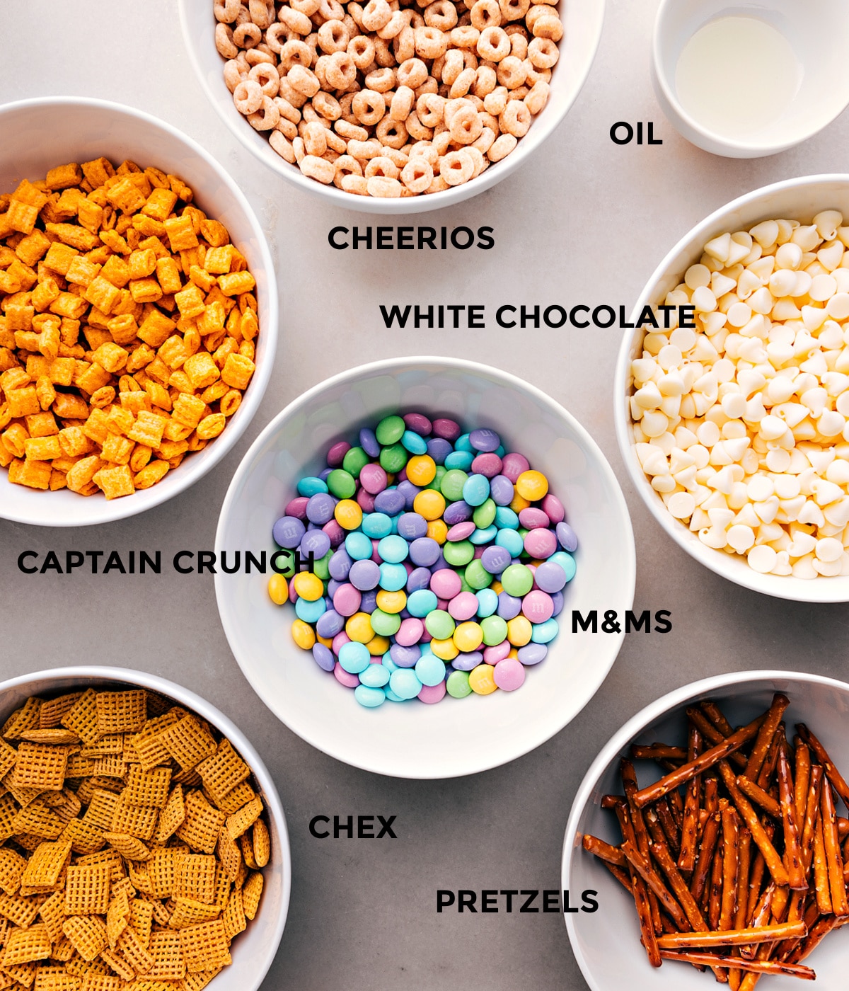 Ingredients In Bunny Bait Recipe All the ingredients prepped and ready for easy assemblyโCheerios, oil, white chocolate, Capโn Crunch, M&Ms, pretzels, and Chex cereal.