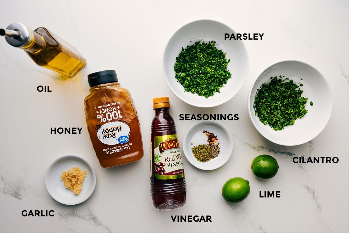 Ingredients In Chimichurri Chicken Ingredients prepped for easy assembly, including oil, honey, garlic, seasonings, parsley, cilantro, limes, and vinegar.